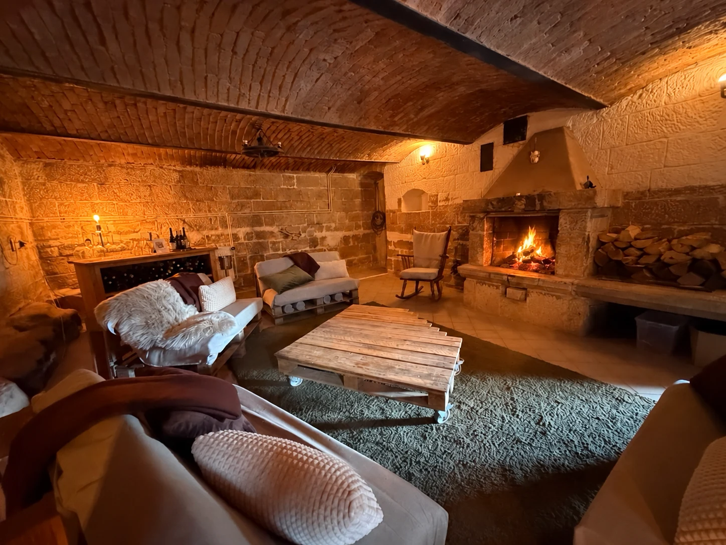 Dear Hill fireplace and wine room with a vaulted brick ceiling, stone walls, sofas and a lit fireplace.