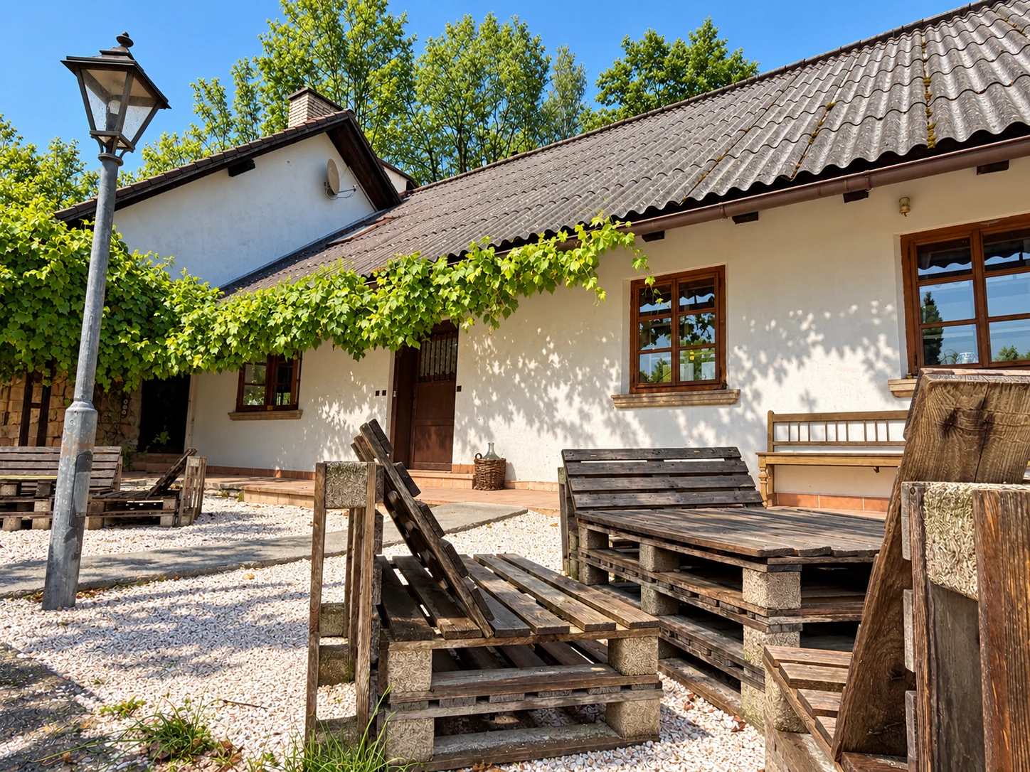 Dear Hill main house with a vine-covered white facade, wooden windows and outdoor seating in a gravel courtyard.