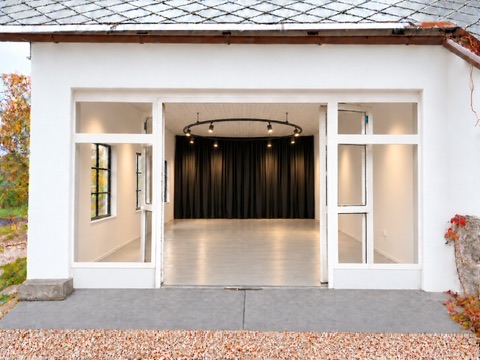 View through the open glass doors into the Dear Hill workshop studio, with an open floor, dark curtains and a circular ceiling light.